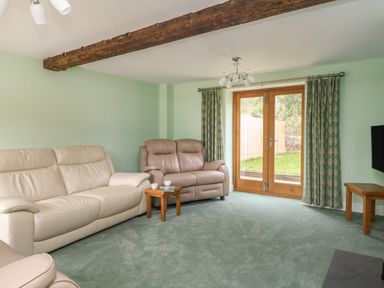 A living room with leather sofas wooden tables and glass doors leading outside at The Granary Burton Bradstock