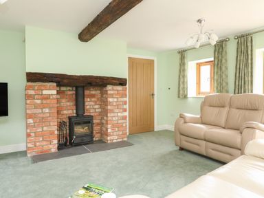 A living room with a brick fireplace and wood burning stove two beige sofas green curtains and a wooden door at The Granary Burton Bradstock