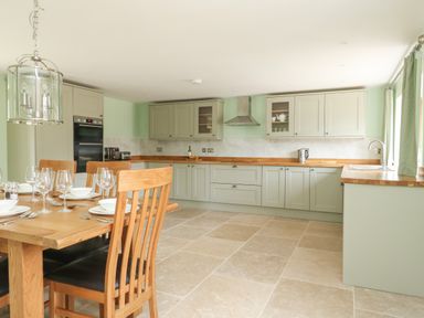 A kitchen with wooden dining table and chairs set with plates and glasses at The Granary Burton Bradstock