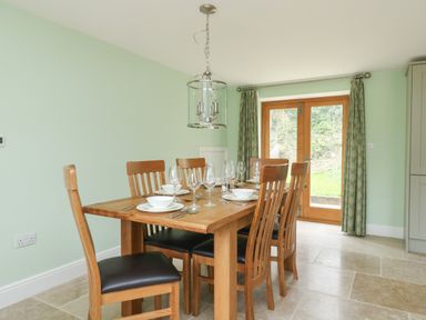 A dining room with a wooden table set with plates bowls glasses and cutlery six wooden chairs and glass doors with curtains at The Granary Burton Bradstock