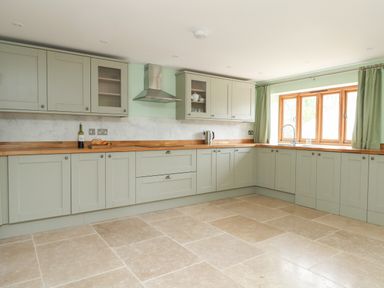 A kitchen with green cabinets wooden countertops tiled floor and a window with green curtains at The Granary Burton Bradstock