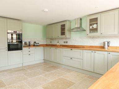 A kitchen with light gray cabinets wooden countertops built in oven toaster and kettle at The Granary Burton Bradstock