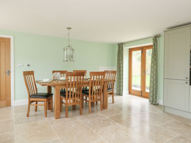 A dining area with a wooden table and six chairs with plates and glasses next to a wooden door and green curtains at The Granary Burton Bradstock