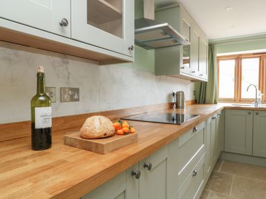 A kitchen with wooden counters a bottle of wine bread small tomatoes a kettle and a window at The Granary Burton Bradstock