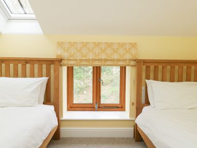 A bedroom with two wooden beds and a window with a patterned blind at The Granary Burton Bradstock