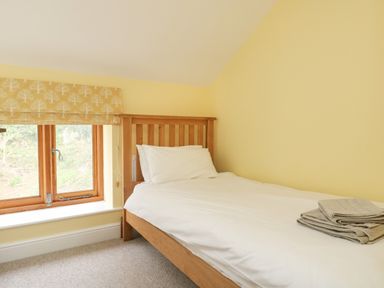 A bedroom with a single wooden bed white bedding folded towels on the bed and a window with patterned blind at The Granary Burton Bradstock