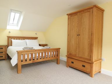 A bedroom with a wooden bed with white bedding and two bedside tables and a wooden wardrobe at The Granary Burton Bradstock