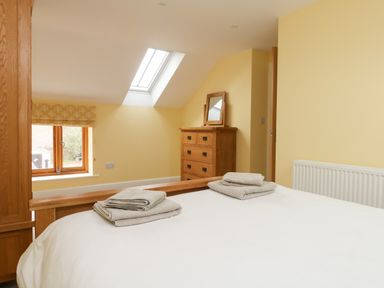 A bedroom with a bed with towels on it a wooden chest of drawers with a mirror and a skylight window at The Granary Burton Bradstock