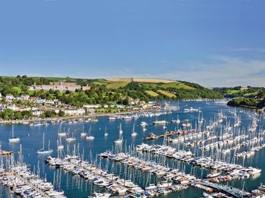 A marina with many boats docked on water near a town with green hills in the background at Fairhaven in Dartmouth