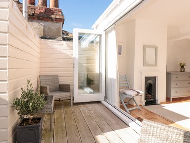 A small outdoor patio with wicker chairs and a potted plant opening to a room with a wooden floor a chair with a cushion a fireplace and a dresser at Fairhaven in Dartmouth