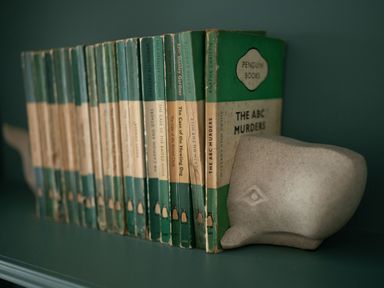 A row of vintage green penguin books supported by a whale-shaped bookend on a green shelf at Fairhaven in Dartmouth