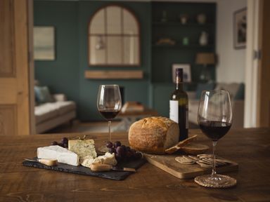 A wooden table with cheese grapes bread crackers wine glasses and a bottle in a living room at Fairhaven Dartmouth