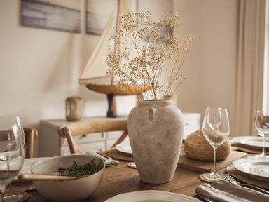 A dining table set with a vase of dried flowers a bowl of greens bread plates and wine glasses at Fairhaven in Dartmouth