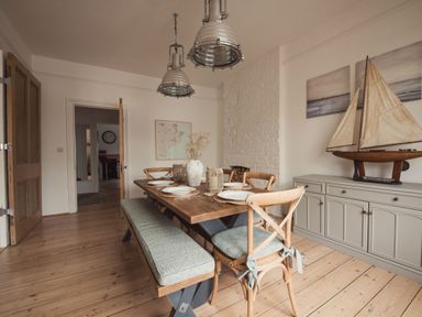 A dining room with a wooden table set with plates and chairs a model sailboat on a sideboard and pendant lights at Fairhaven in Dartmouth