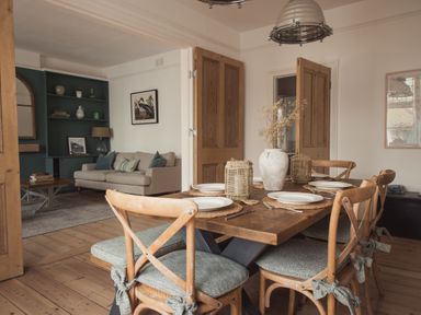 A dining room with a wooden table set with plates and a living room with a beige sofa in the background at Fairhaven Dartmouth