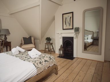 A bedroom with a bed rolled towels a fireplace a large mirror an armchair a small table and wooden floor at Fairhaven in Dartmouth