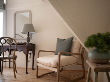 A wooden armchair with cushions next to a wooden desk with a lamp and a mirror on the wall in a room at Fairhaven in Dartmouth