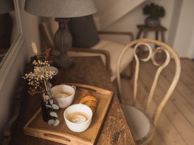 A wooden tray with two cups of coffee a croissant and a small vase with dried flowers on a wooden table with a chair and lamp nearby at Fairhaven in Dartmouth