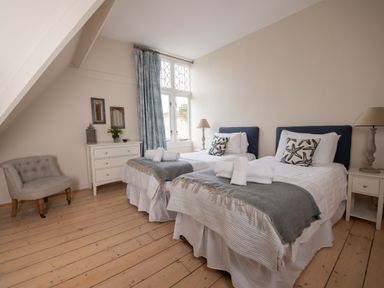 A bedroom with two single beds a chair a chest of drawers and a window with curtains at Fairhaven in Dartmouth