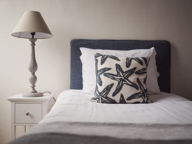 A bed with white pillows and a starfish patterned cushion next to a white bedside table with a lamp at Fairhaven in Dartmouth