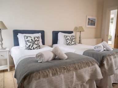A bedroom with two single beds side by side each with a blue headboard white bedding patterned pillows grey throws towels on the beds bedside tables and lamps at Fairhaven in Dartmouth