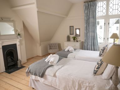 A bedroom with two single beds a fireplace a chair and windows with blue curtains at Fairhaven in Dartmouth