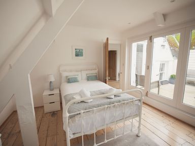 A bedroom with a white bed and pillows next to a nightstand with a lamp and large glass doors at Fairhaven in Dartmouth