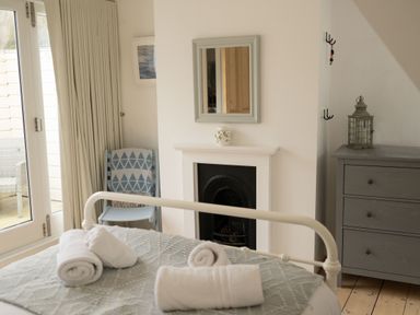 A bedroom with a bed, rolled towels, a chair with a blanket, a fireplace, a mirror, and a dresser at Fairhaven in Dartmouth