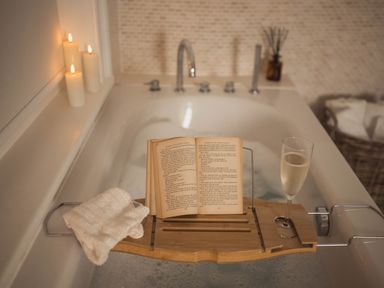 A bathtub with lit candles on the edge a wooden bath tray holding an open book a white cloth and a glass of champagne at Fairhaven in Dartmouth