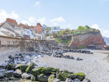 A pebble beach with large rocks and a sea wall next to houses on a cliff at The Retreat in Washford near Williton