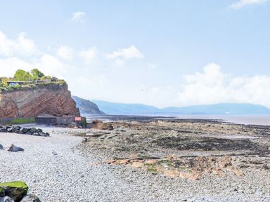 A rocky beach with cliffs and houses on top near the sea at The Retreat in Washford near Williton