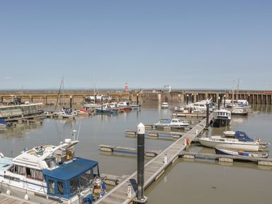 A harbor with multiple boats docked at wooden piers and a red lighthouse in the background at The Retreat in Washford near Williton