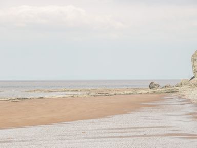 A sandy beach with rock formations and calm sea at The Retreat in Washford near Williton