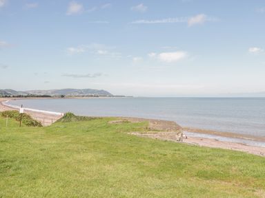 A grassy area leading to a beach with calm sea and hills in the background at The Retreat in Washford near Williton
