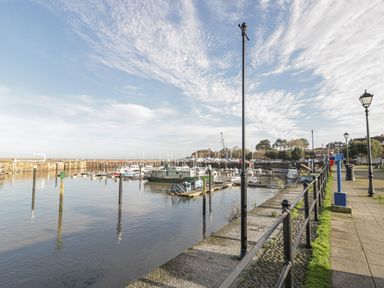 A harbor with boats docked along piers and a walkway with street lamps and railings at The Retreat in Washford near Williton