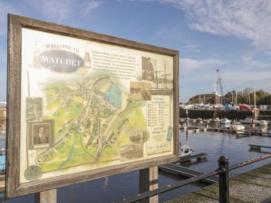 A wooden framed welcome sign with a map and information about Watchet by a marina with boats and a crane at The Retreat in Washford near Williton
