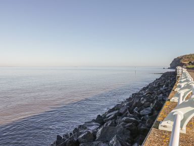 A coastal scene with a rocky shoreline and a white railing along a walkway at The Retreat in Washford near Williton