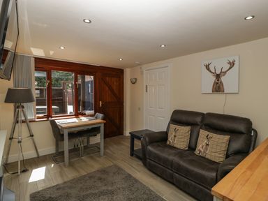 A living room with a dark sofa and animal cushions a small dining table with two chairs and a tripod lamp at The Retreat in Washford near Williton