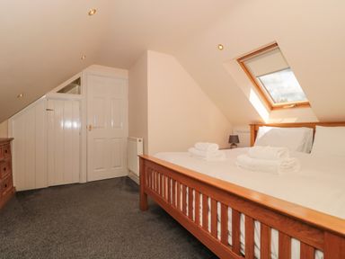 A bedroom with a wooden bed, folded towels on the bed, a small bedside lamp, a skylight window, a white door, and carpeted floor at The Retreat Washford near Williton