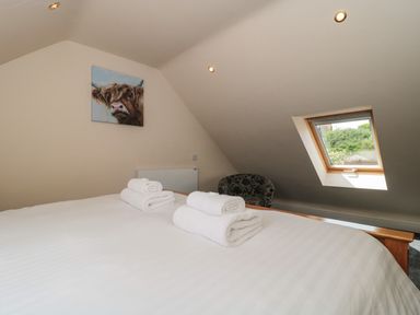 A bedroom with a sloped ceiling a bed with white linens and folded towels a window and a chair at The Retreat in Washford near Williton