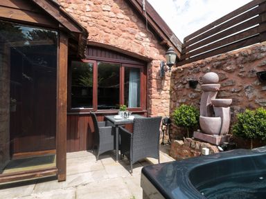 An outdoor patio with a table and two chairs near a stone wall and a fountain at The Retreat in Washford near Williton
