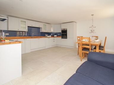 A kitchen with white cabinets wooden countertops blue backsplash and a dining table with wooden chairs at The Stables Burton Bradstock
