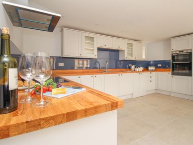 A kitchen with wooden countertops white cabinets a bottle of wine two wine glasses and vegetables on the counter at The Stables Burton Bradstock