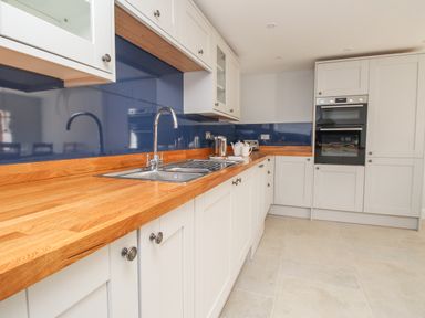 A kitchen with white cabinets wooden countertop blue backsplash and a double oven at The Stables Burton Bradstock