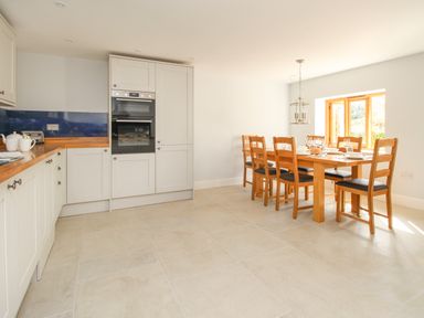 A kitchen with white cabinets wooden countertop and dining table with chairs near a window at The Stables Burton Bradstock