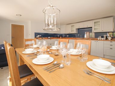 A dining table set with plates bowls glasses and cutlery in a kitchen with wooden countertops and white cabinets at The Stables Burton Bradstock