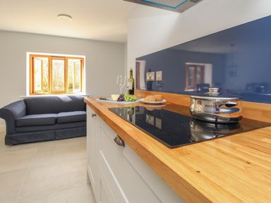 A kitchen area with a wooden countertop stove pot couch and open window at The Stables Burton Bradstock