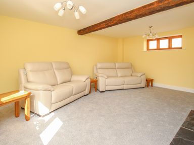 A living room with two beige sofas wooden side tables and a wooden beam on the ceiling at The Stables Burton Bradstock