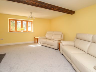 A living room with two beige sofas a window with flowers and wooden beams at The Stables Burton Bradstock
