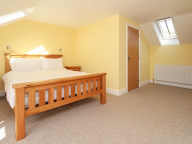 A bedroom with a wooden bed frame a wooden door a radiator and skylight windows at The Stables Burton Bradstock